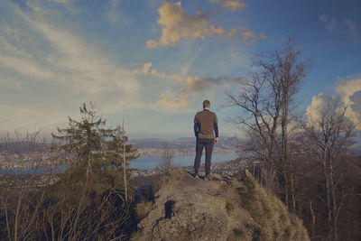 Rear view of man standing on rock against sky