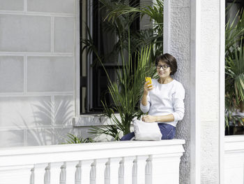 Woman texting on smartphone. pretty female sits on balcony with palm trees in flower pots. 