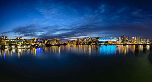 Illuminated city by sea against sky at night