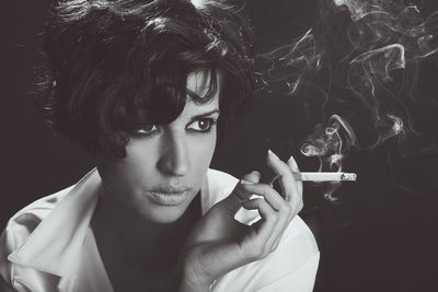 Young woman smoking cigarette against black background