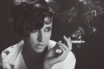 Young man smoking cigarette against black background