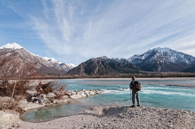 Rear view of man standing at riverbank during winter