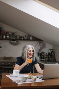 Portrait of laughing senior woman using laptop at breakfast table