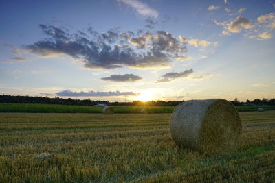 Hay bales on field against sky during sunset