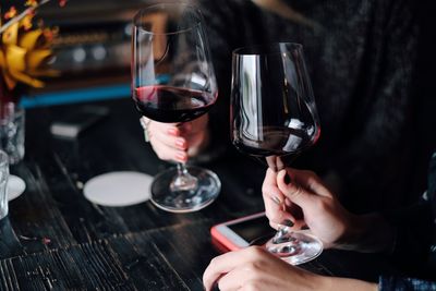 Cropped hands of women toasting red wine at restaurant