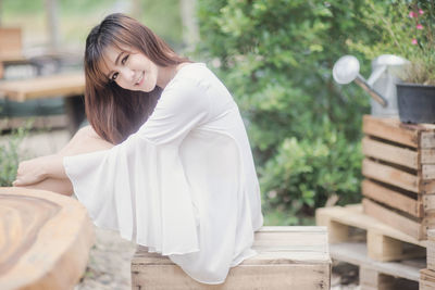 Young woman sitting on crate against plants