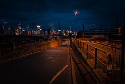 Illuminated street lights on bridge in city against sky at night
