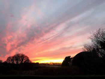 Silhouette trees on field against romantic sky at sunset