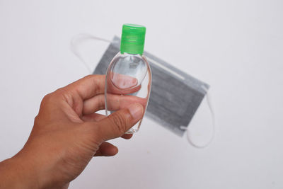 Close-up of hand holding bottle against white background