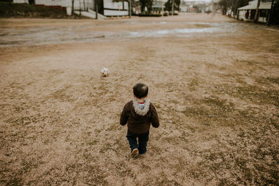 Rear view of boy walking towards soccer ball on land