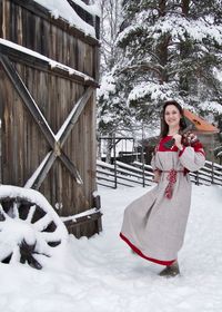 Portrait of woman holding balalaika standing against trees during winter