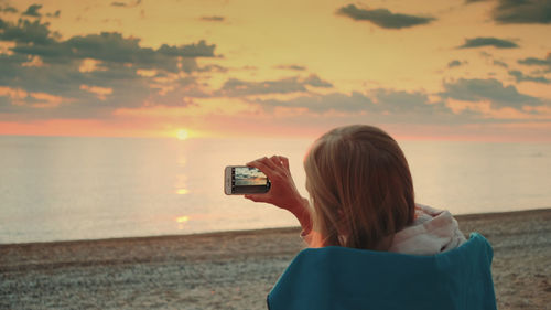 Rear view of woman photographing sea during sunset