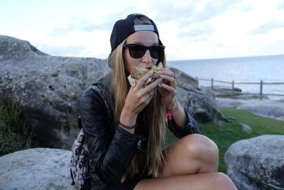 Portrait of woman eating sandwich while sitting at beach