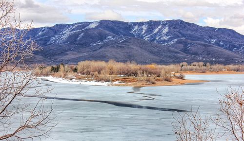 Scenic view of snowcapped mountains next to frozen lake against cloudy sky