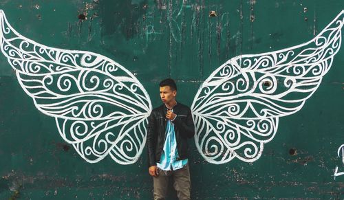 Portrait of man standing by graffiti on wall