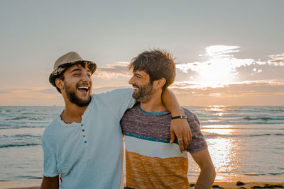 Friends enjoying at beach against sky during sunset