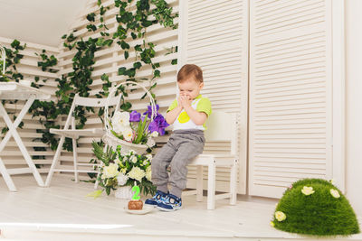 Cute boy sitting on potted plant at home