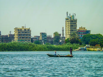 People boating on river against buildings