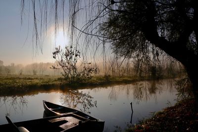 Silhouette boat moored in lake against sky