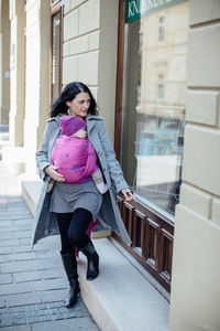 Full length of woman carrying son in scarf outside store