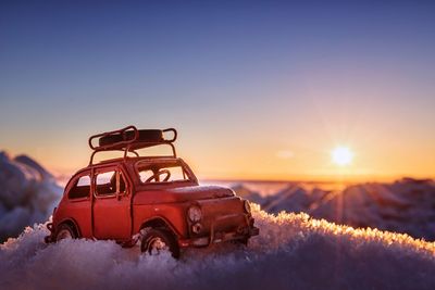 Toy car on frozen field against sky during sunset