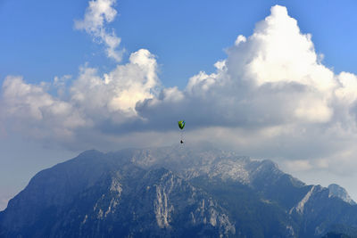 Person paragliding over mountains against sky