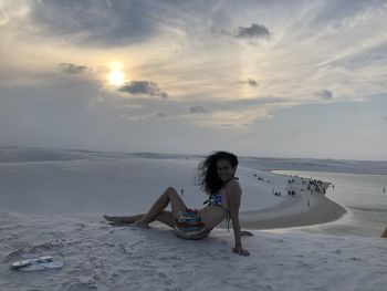 Woman sitting on beach against sky during sunset