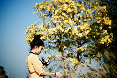 Woman using camera while standing against tree