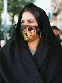 Young woman wearing mask looking away while standing outdoors