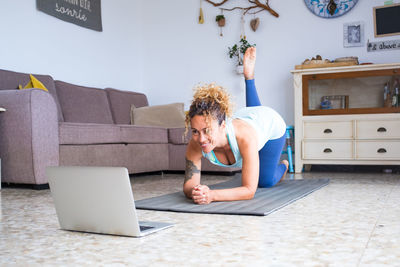 Full length of woman looking at laptop while exercising in living room