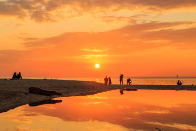 Silhouette people on beach against sky during sunset