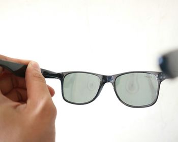 Close-up of hand holding sunglasses against white background