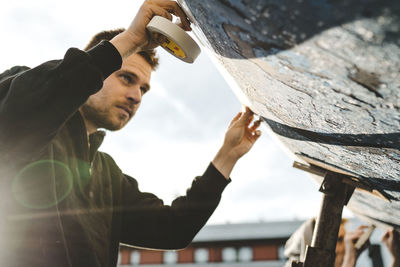 Portrait of young man holding wood against sky