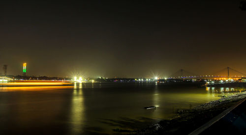 Illuminated city by river against sky at night