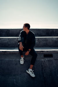 Young man sitting on wall against sky