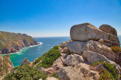 Scenic view of rocks by sea against blue sky