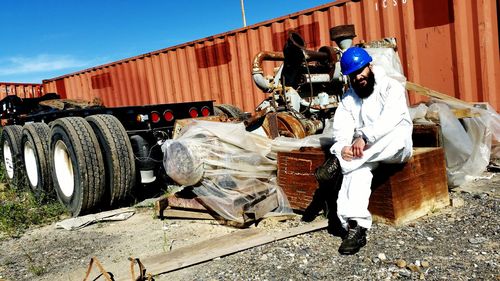 Worker sitting on box by machinery and cargo container