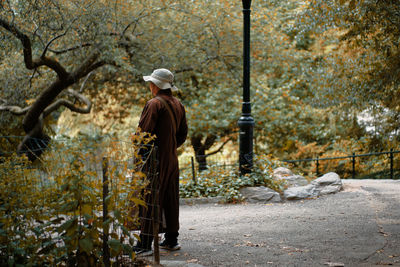 Rear view of a monk standing by plants in central park