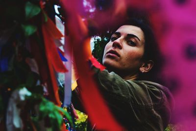 Portrait of smiling young woman standing amidst colorful ribbons on tree