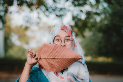 Portrait of teenage girl covering mouth with dry leaf 