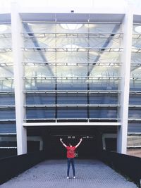 Rear view of man standing on walkway against glass building