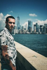 Portrait of young man standing in city against sky