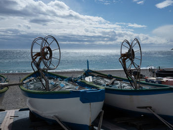 Fishing boats moored on beach against sky