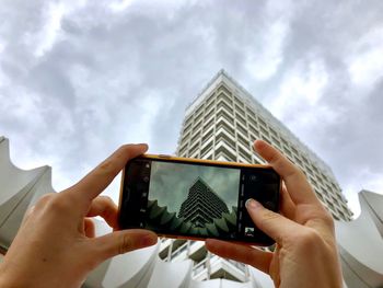 Midsection of person photographing with mobile phone against sky