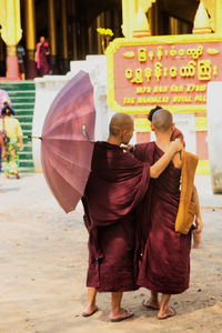 Rear view of monks holding umbrella while standing against temple