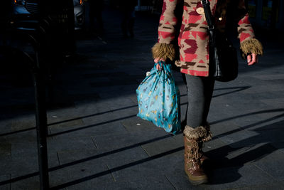 Low section of woman walking on footpath with shopping bag 