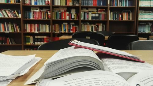 Close-up of books and clipboard on table against bookshelf at library