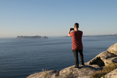 Rear view of person photographing sea against sky