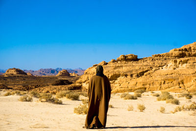 Rear view of man standing on rock against clear blue sky