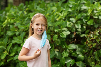Portrait of smiling girl with mask standing against plants